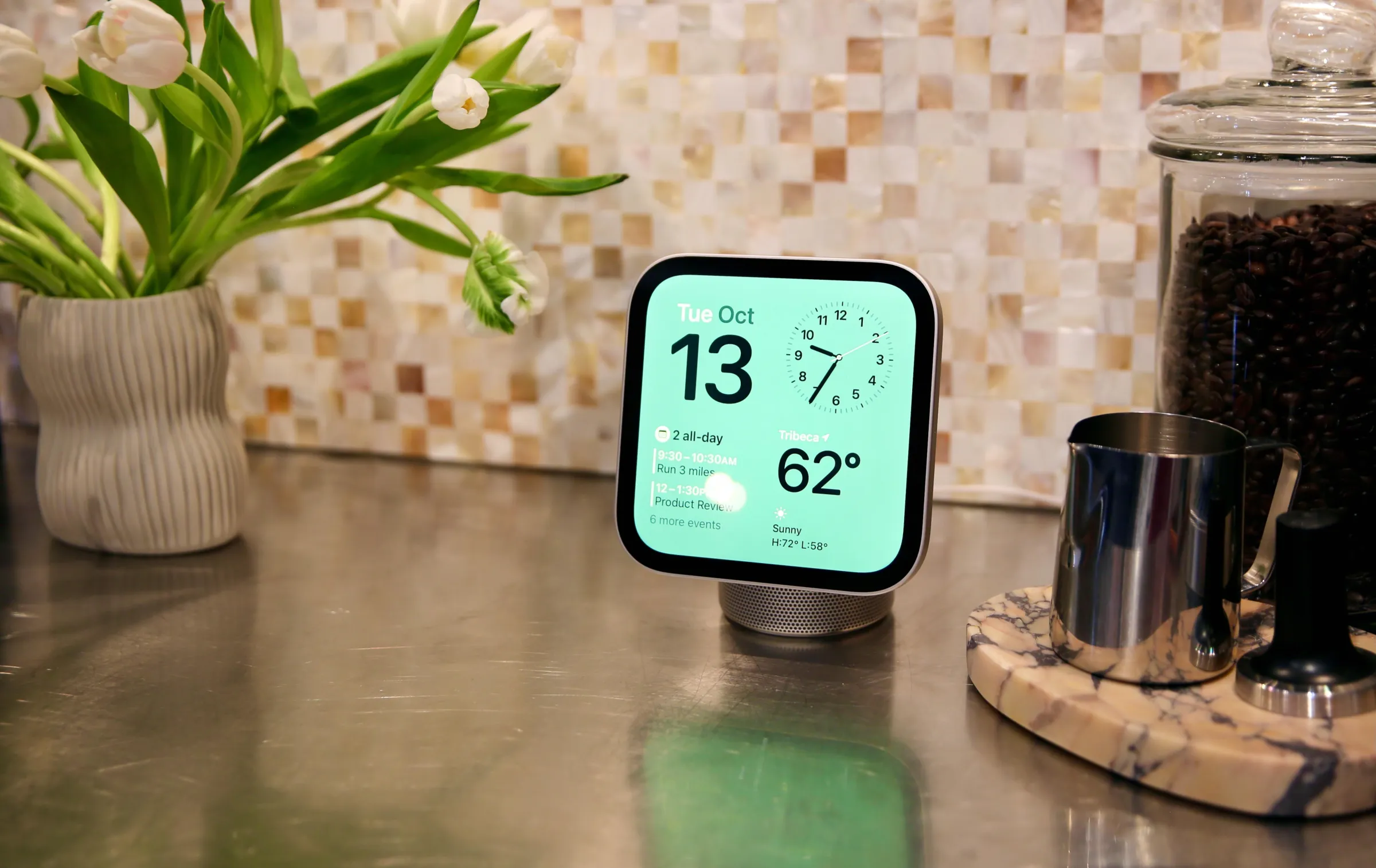 An Apple HomeView is on a kitchen counter. Displayed on the screen are the date, time, weather, and calendar.