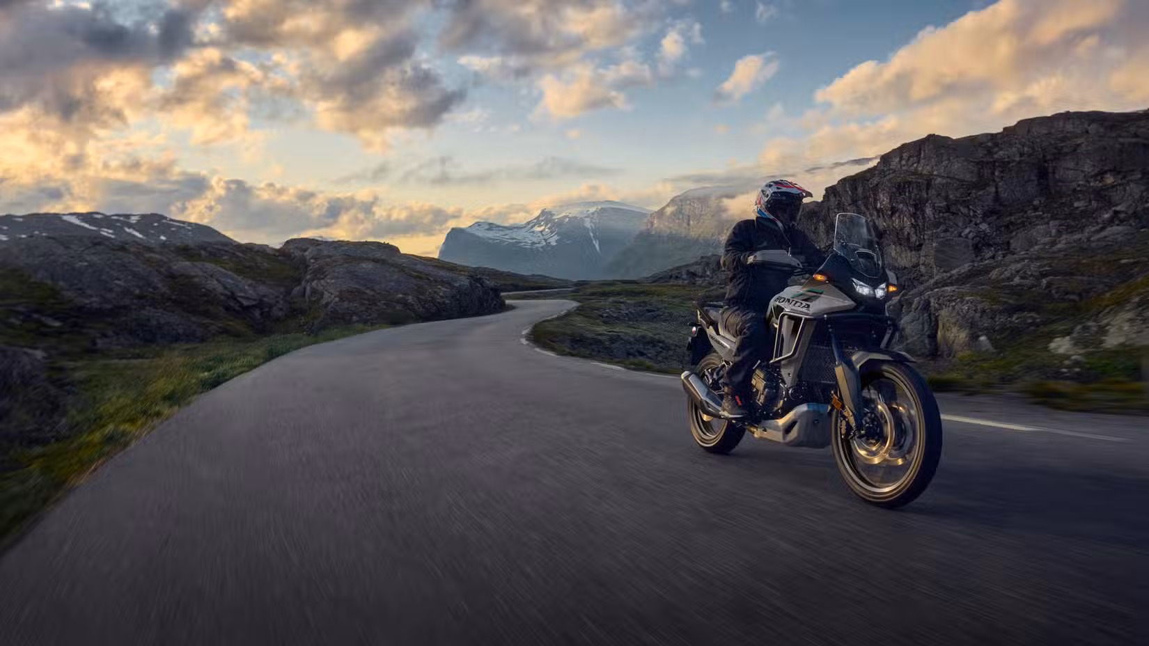 2026 Honda XL750 Transalp riding down a lonely curving road with mountains in the background