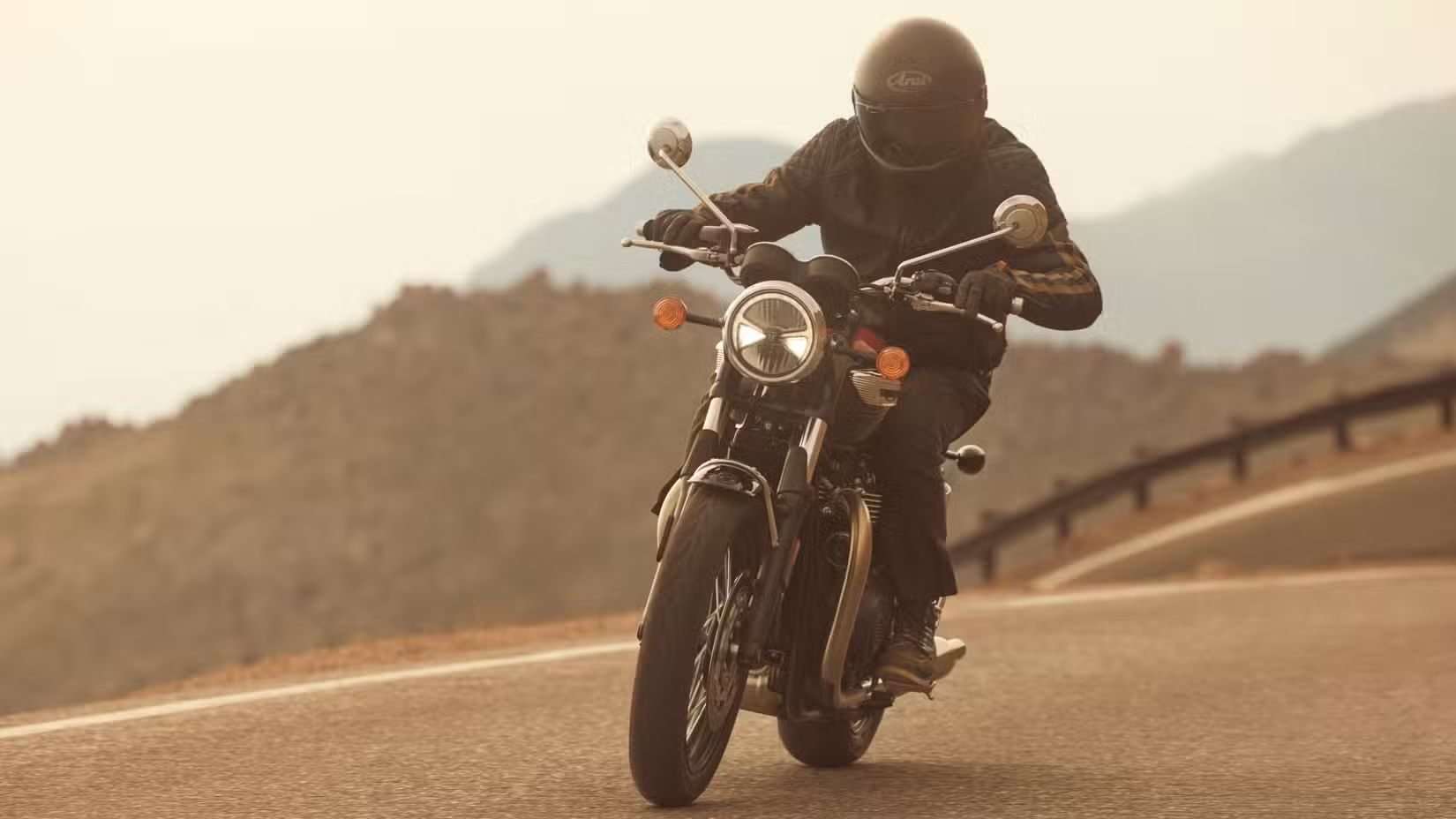 2025 Triumph Bonneville T100 riding along a highway, viewed from the front three-quarter angle.