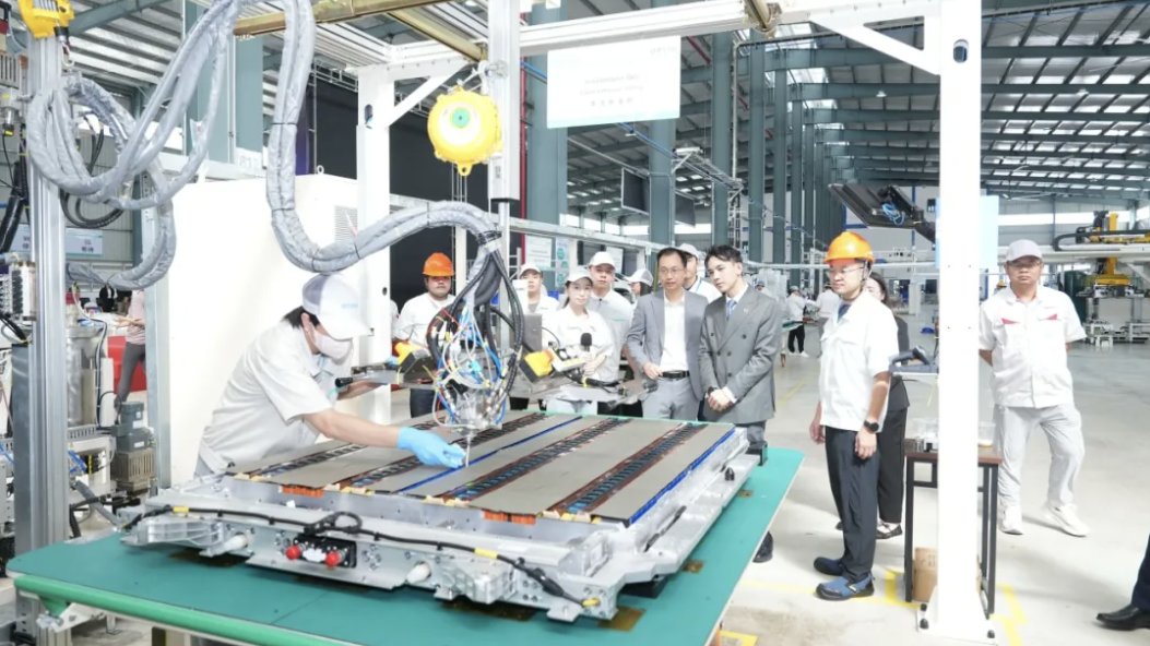 A worker operates equipment over a battery pack as visitors observe the production line at Inpow Battery's Thai plant.