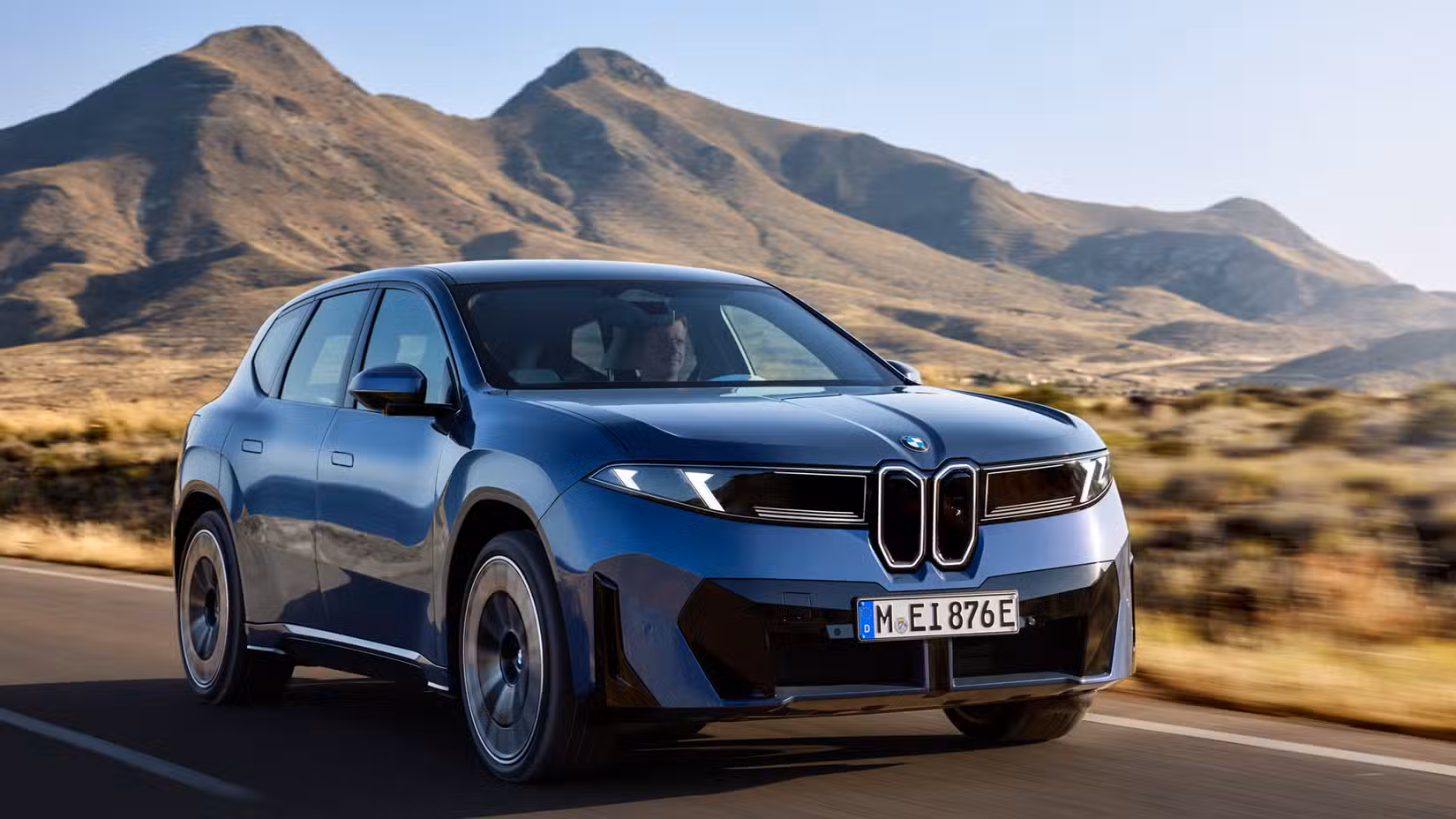 2027 BMW iX3 front third quarter view driving down rural highway
