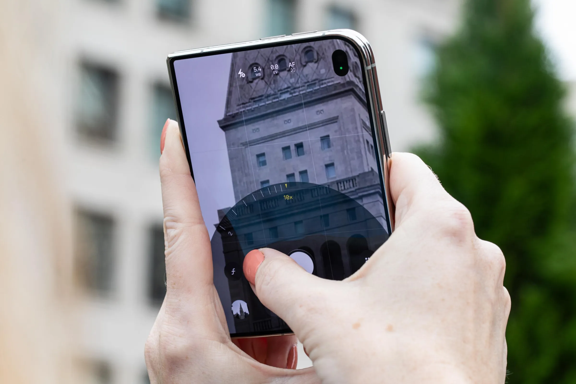 Hands holding a folded iPhone Duo and using the main camera to take a photo. They’re zooming in using the onscreen controls.