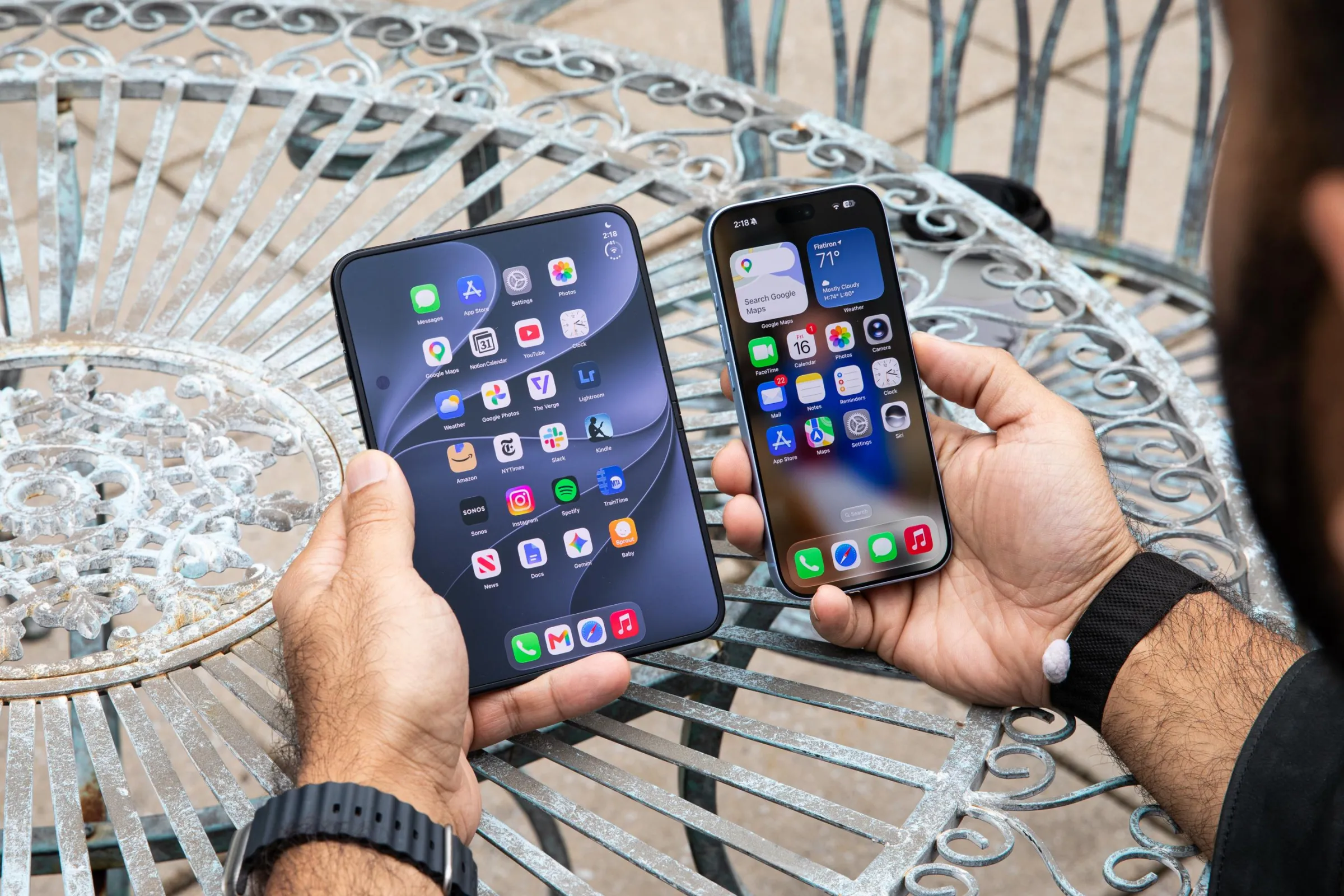 A person holding the iPhone Duo, which is open to its inner screen in portrait orientation, next to a standard modern iPhone to show the size difference. The Duo looks a little less than twice as wide as the regular iPhone.