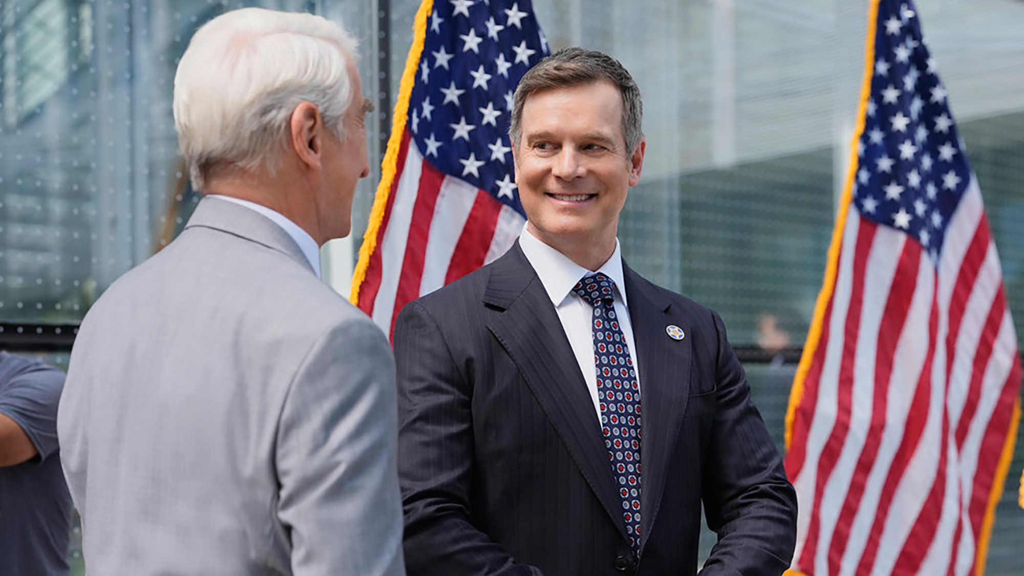 Peter Krause stands in front of two American flags during an episode of Line of Fire