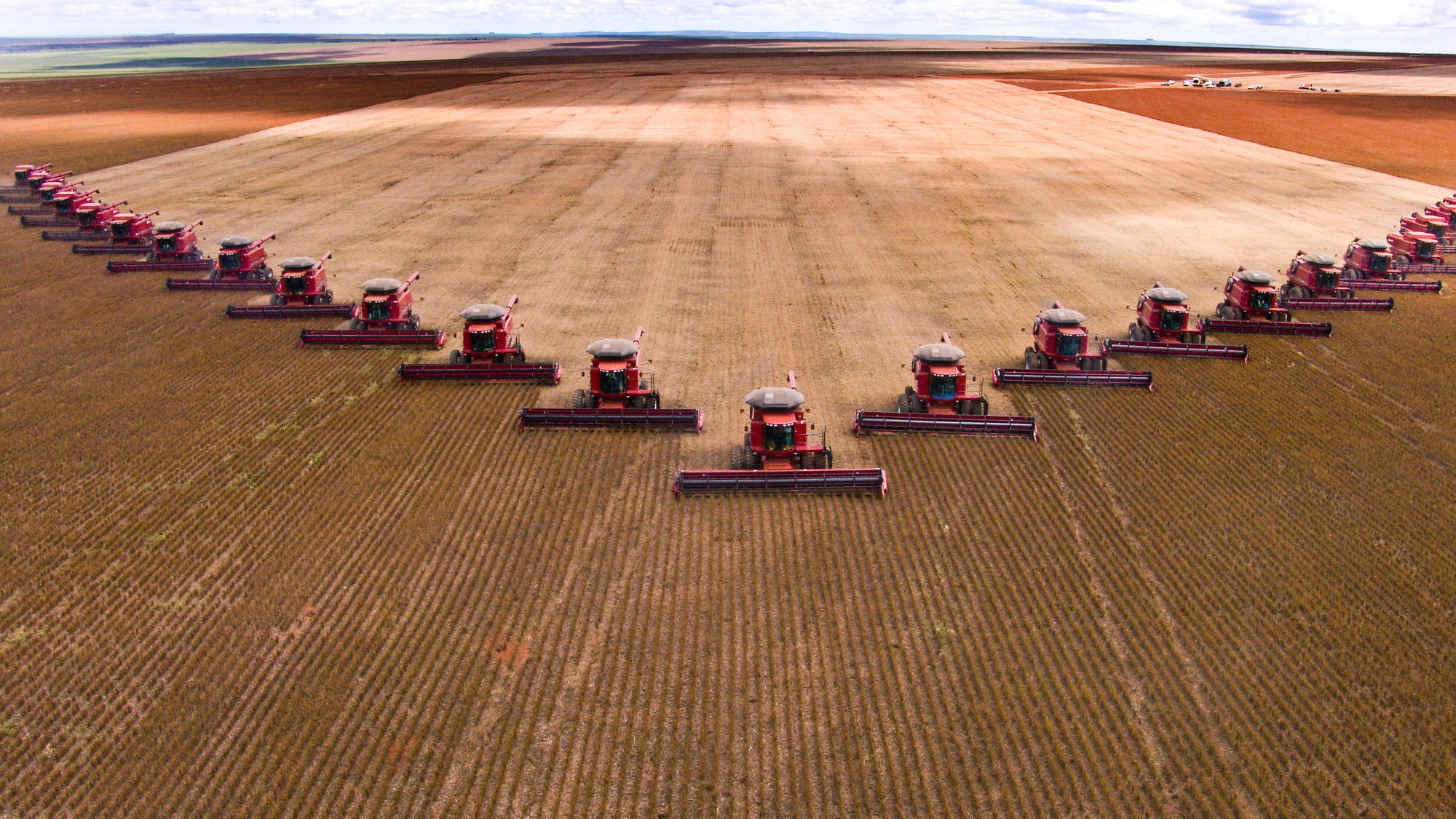 A row of tractors ride through dirt fields