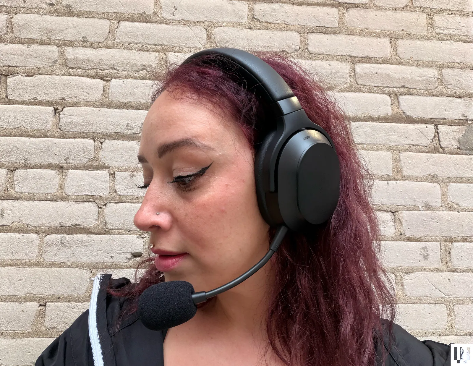 Person with wavy reddish brown hair wearing black headphones with an extended microphone sticking out of one ear piece