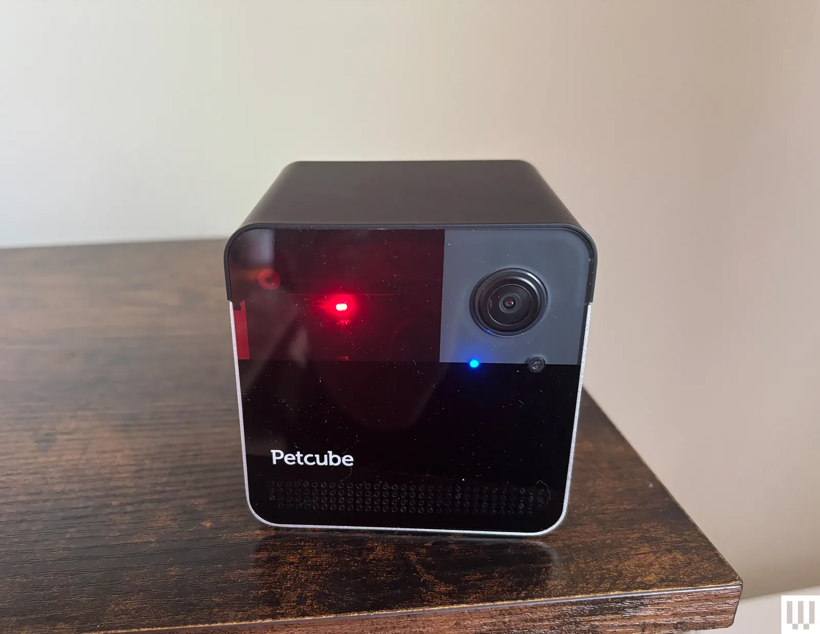Rotating black pet camera with red laser sits on a wood ledge with cream wall background