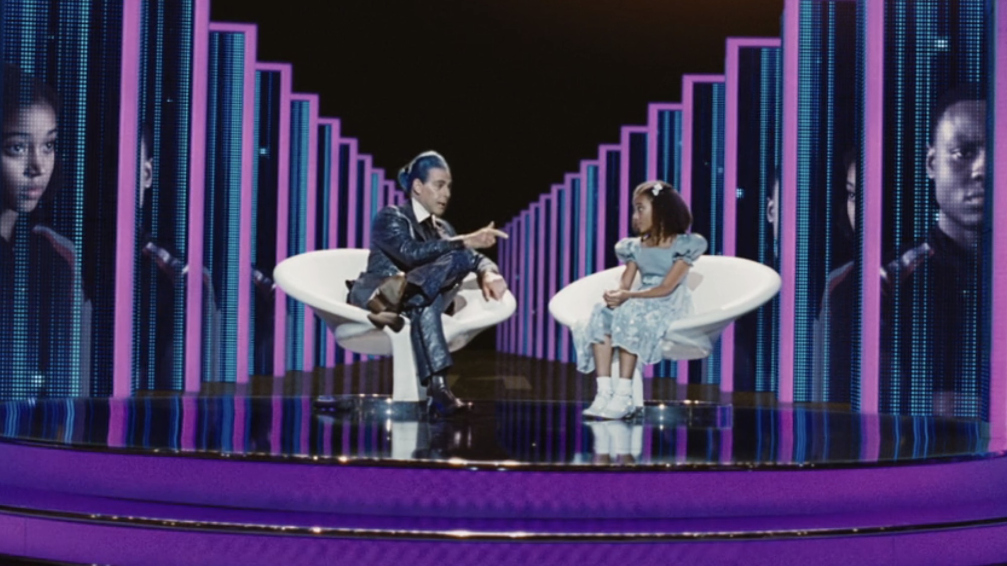 Rue being interviewed by Flickerman in a blue dress during the Hunger Games.