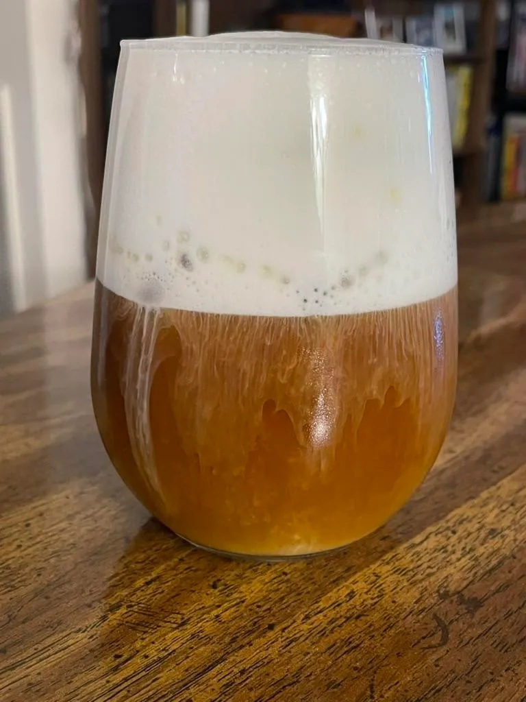 A glass of iced coffee, with a generous white foam top that’s dripping into the coffee.