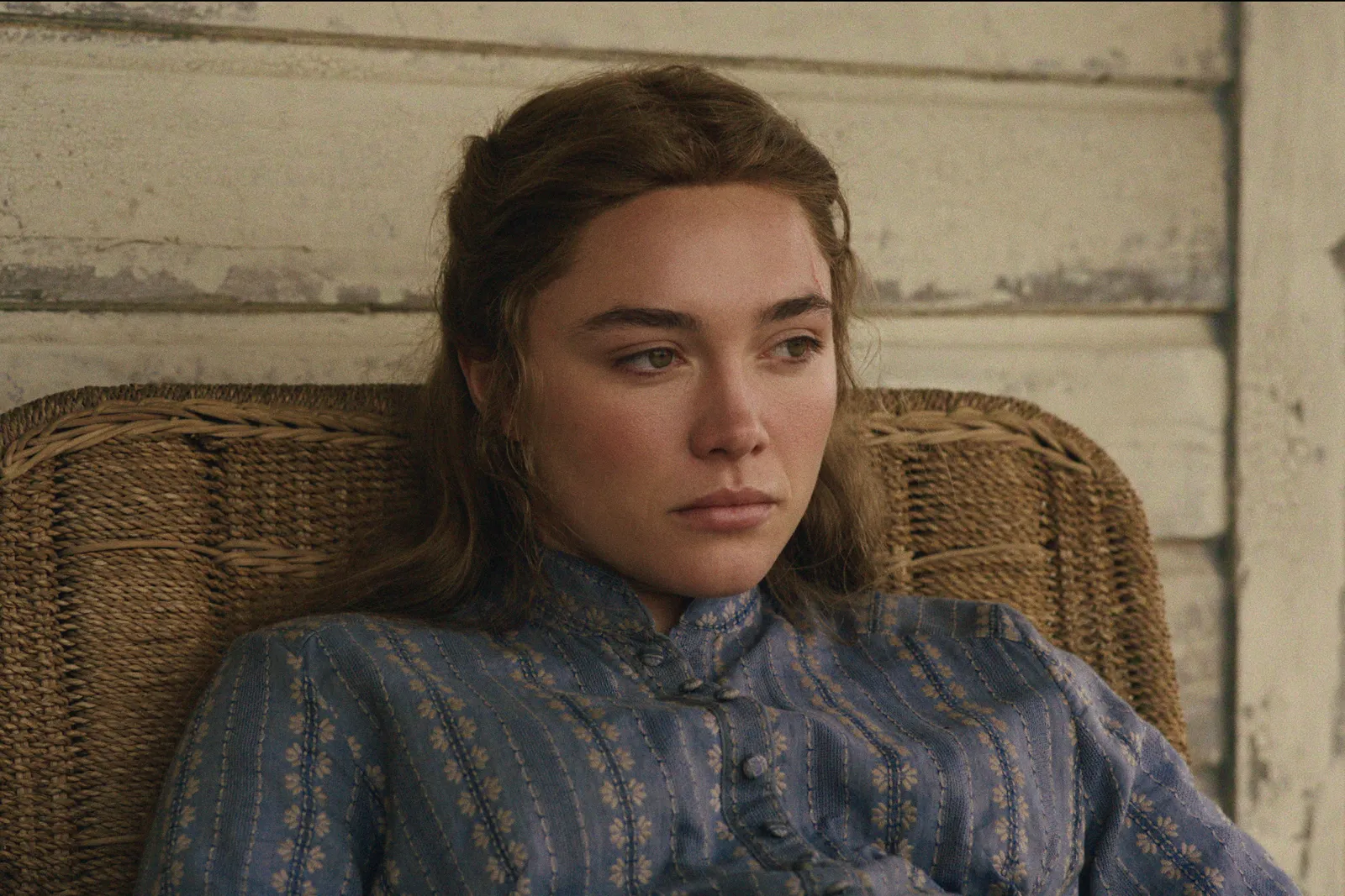 Florence Pugh as Cathy Ames in episode 103 of East of Eden sitting on the front porch in a wicker chair.