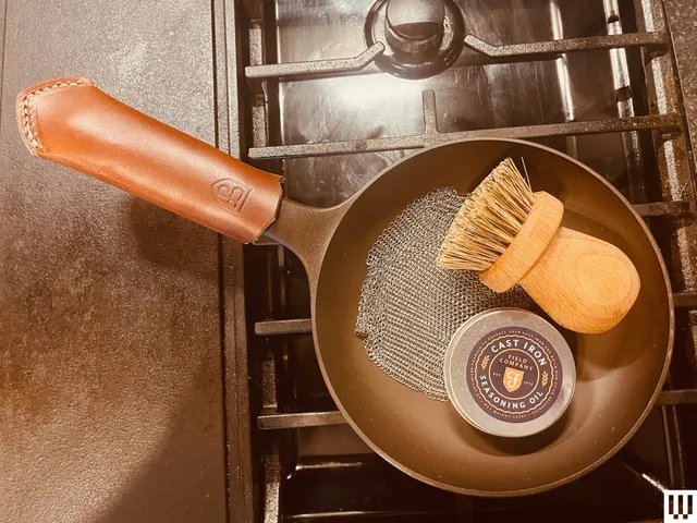 Overhead view of cast iron pan with a leather handle with a brush and tin sitting inside the pan