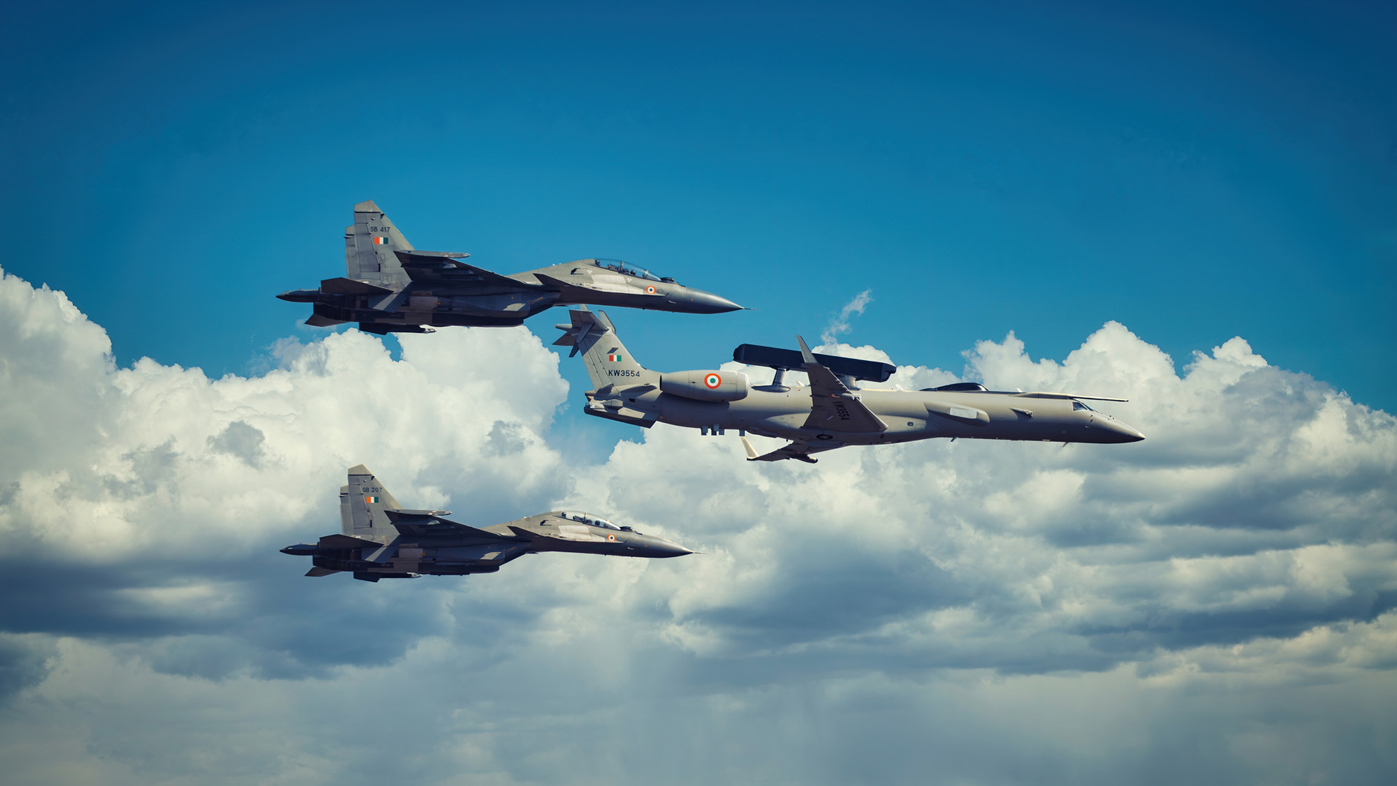 Three gray fighter jets float amidst clouds in the sky.