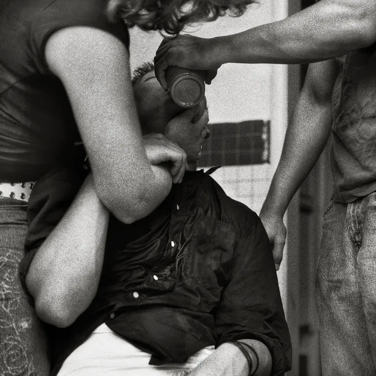 Two men standing above another man, who sits on a toilet without pants. The image is from Andrew Moisey’s photographic collection exploring frats at UC Berkeley in the 2000s.