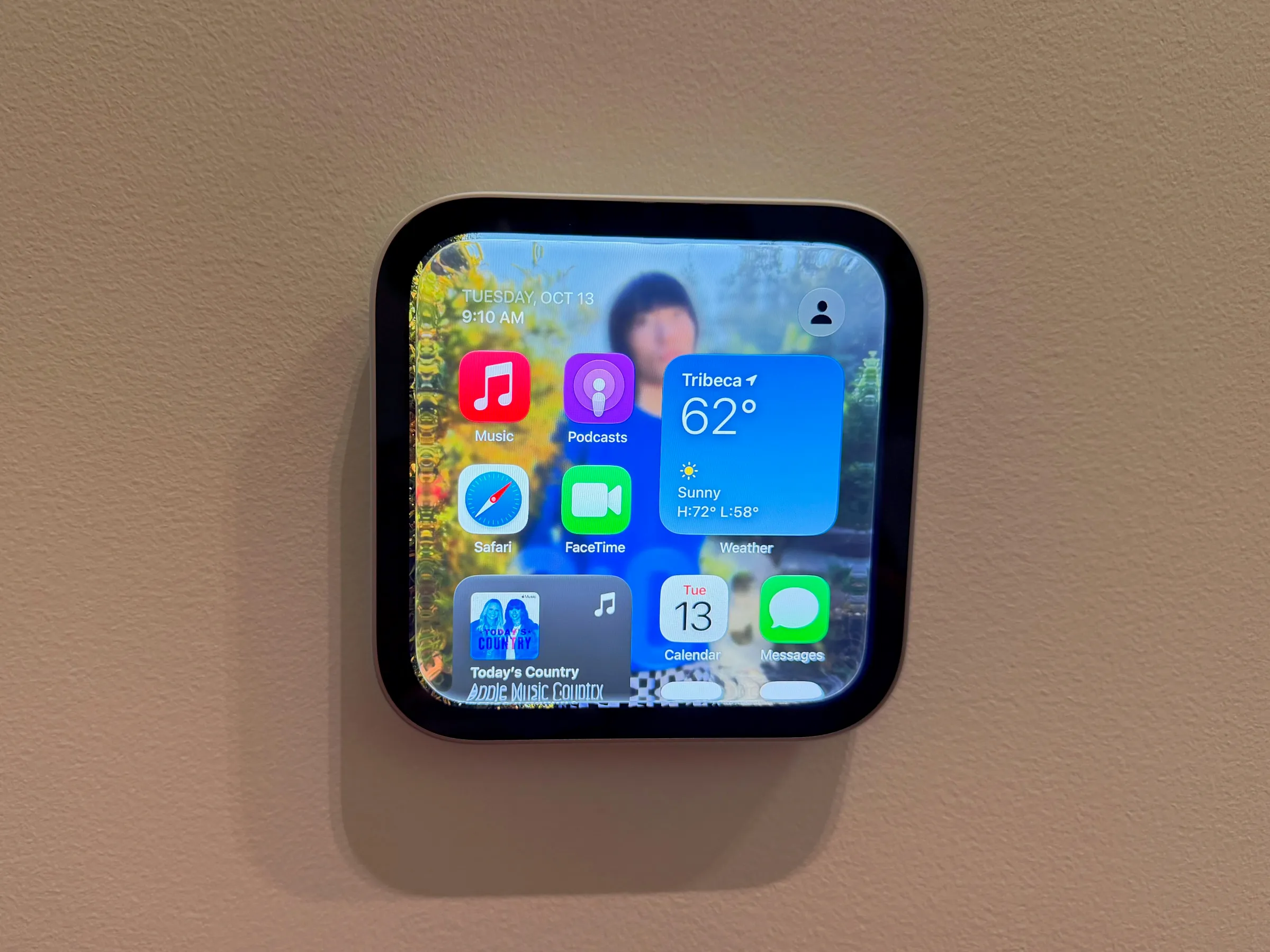 A HomeView mounted on a wall shows the display’s interface, which includes app icons for messages, music, podcasts, FaceTime, and more.