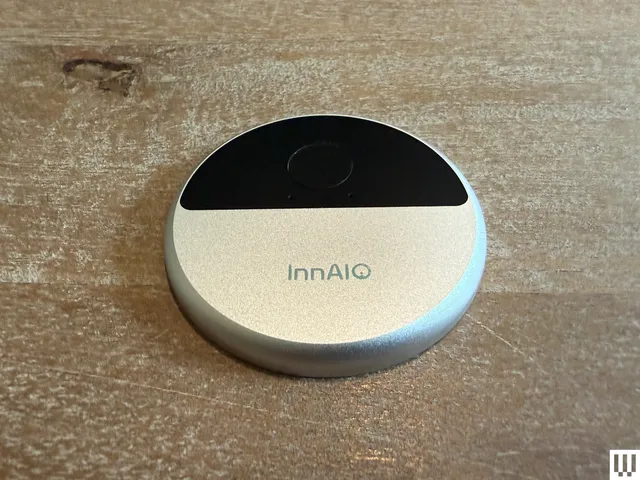 InnAIO AI Translator , a silver and black disc-shaped object on a wooden table