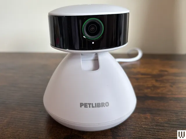 Rotating white pet camera sits on a wood ledge with cream wall background