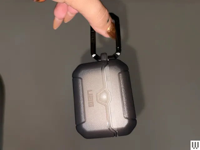 Hand pinching a small rectangular case by the keychain attached