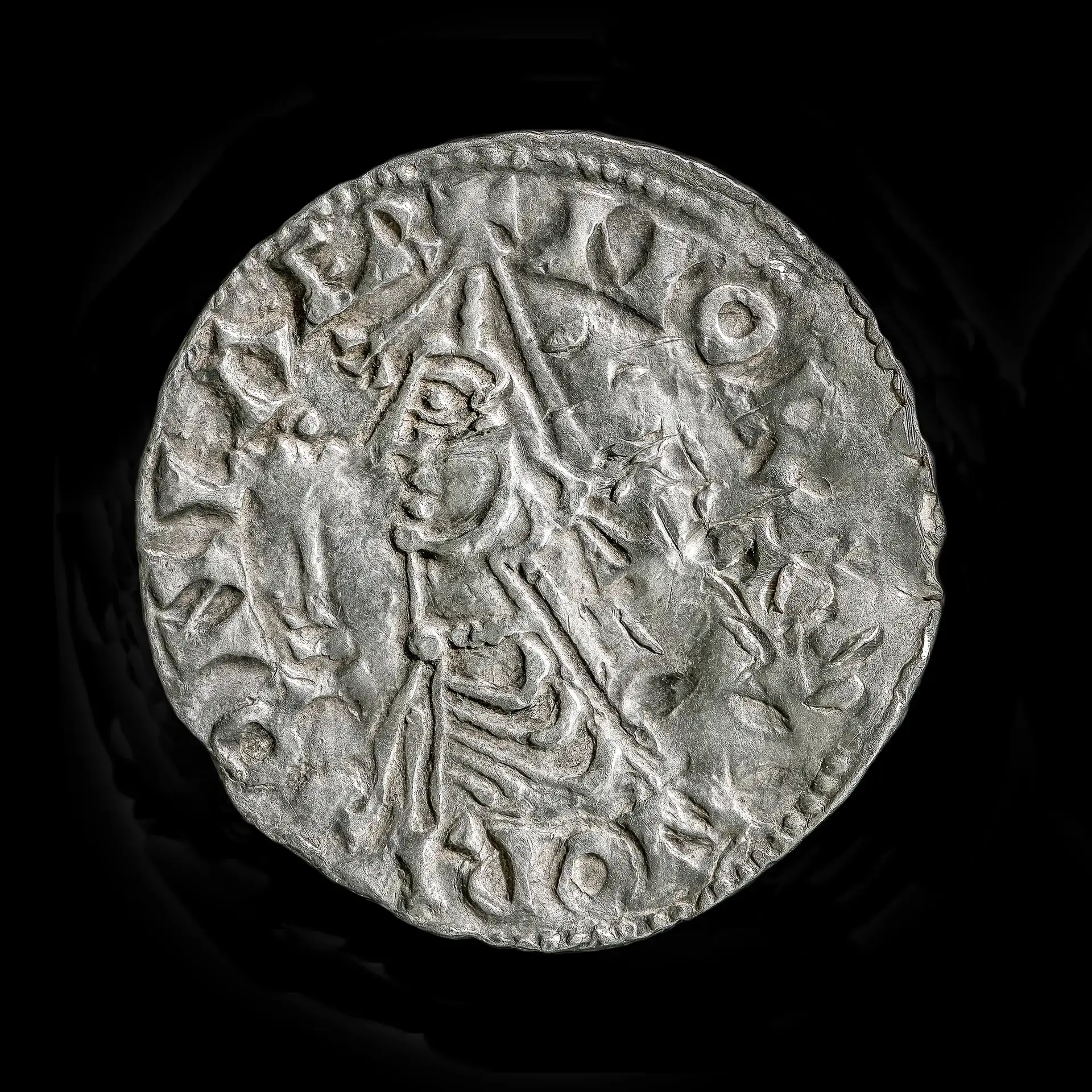 A close up of a silver coin showing a man's profile and writing around the periphery.