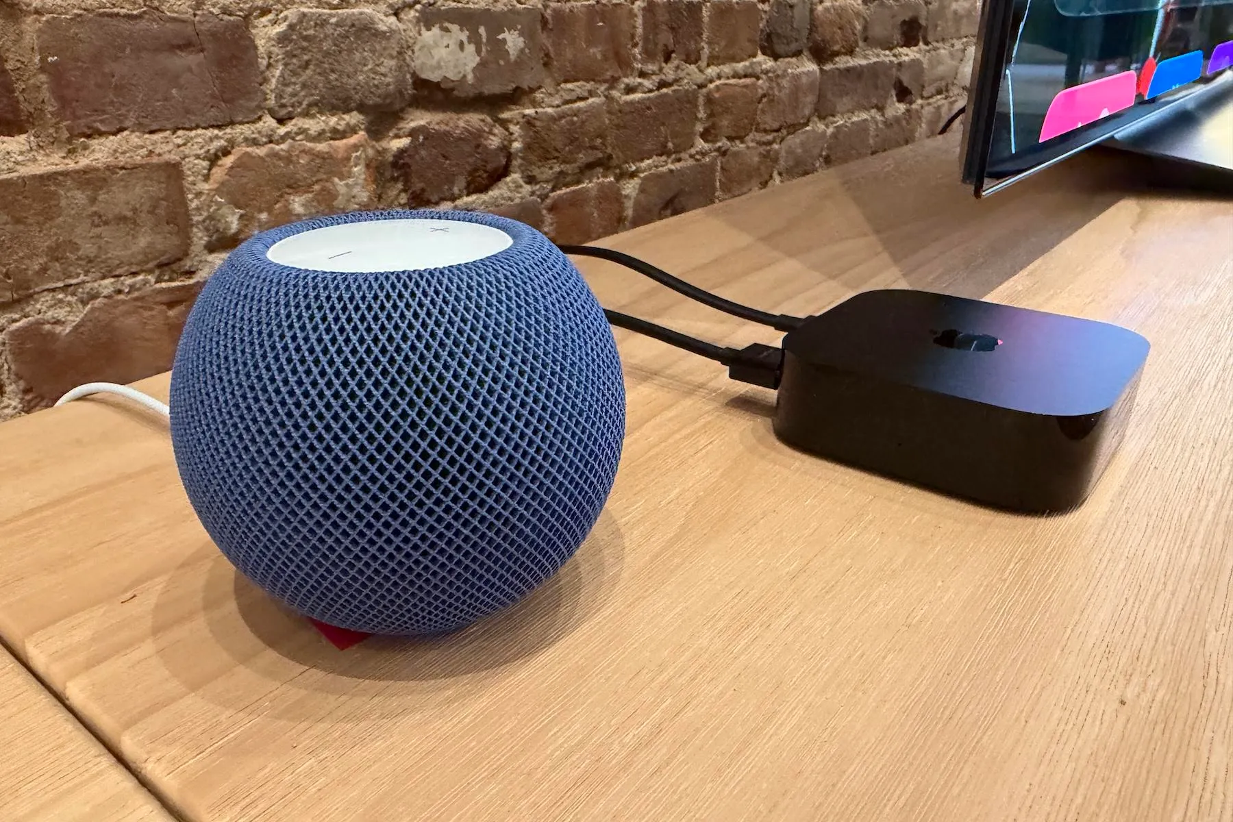 The Apple HomePod Mini 2 and 4th-generation Apple TV 4K on a tan wooden table at the Apple Welcome Home event.