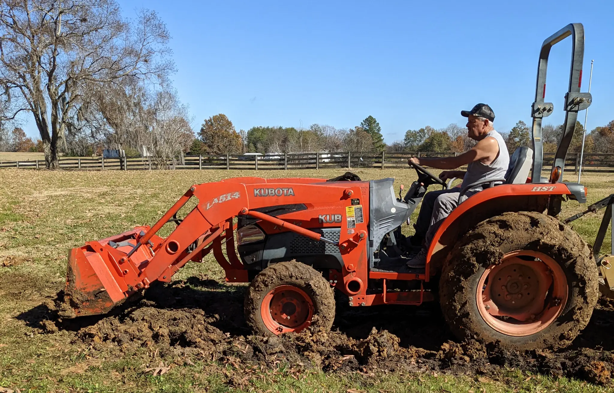 A man, my dad, driving an orange Kubota tractor.