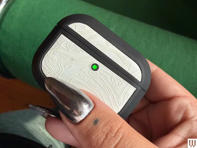 Person's hand pinching a small white case with rounded edges, black trim, and a green light turned on