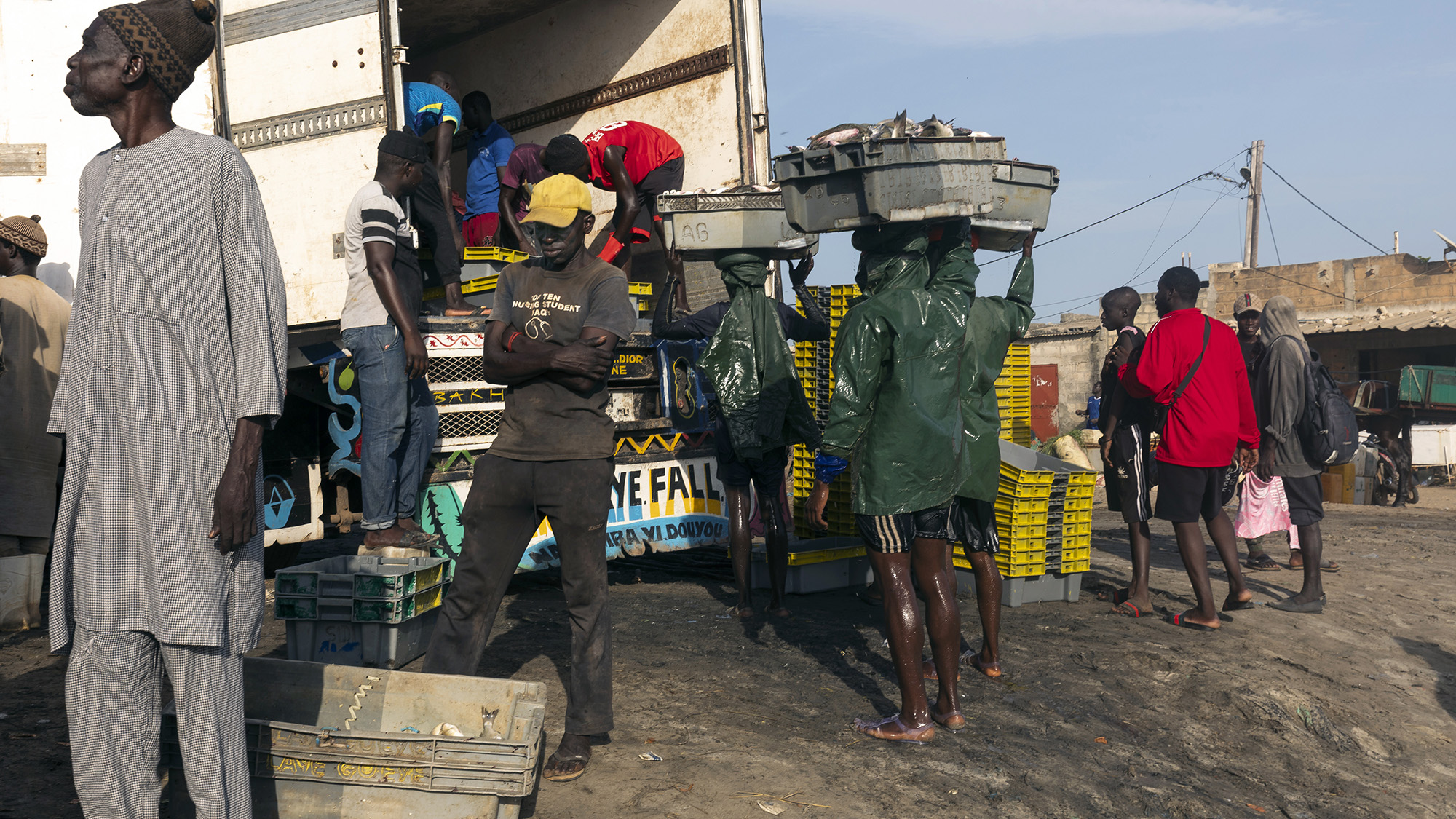 A line of people is seen at a local market with baskets of fish nearby.