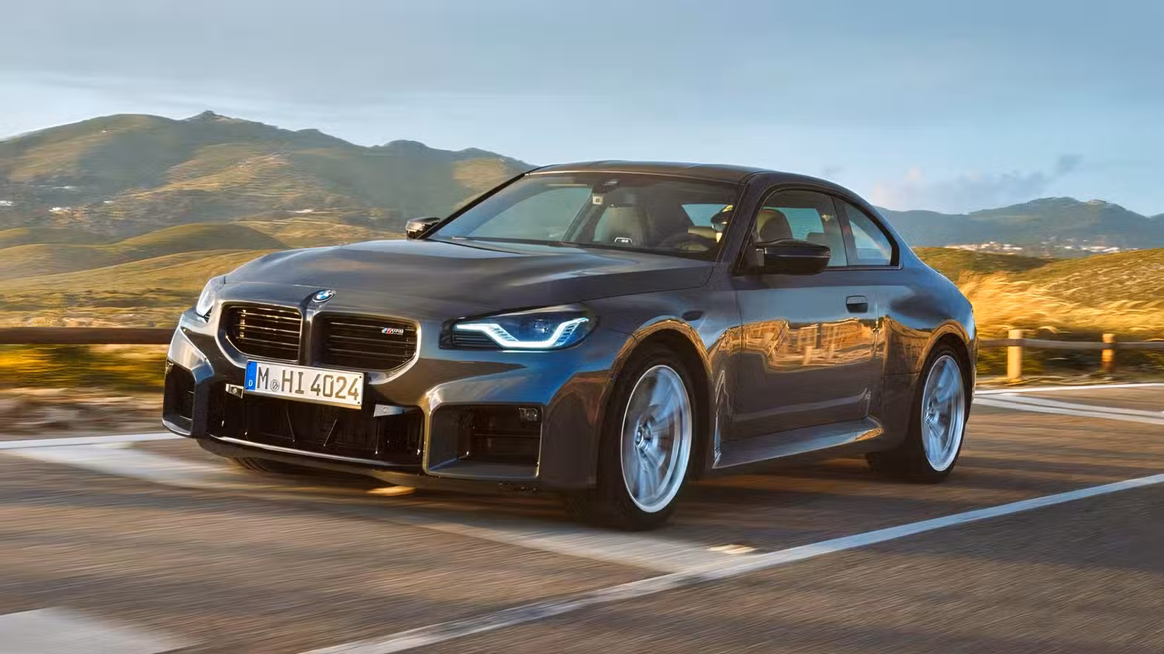 Front 3/4 action shot of 2026 BMW M2 in black driving on road