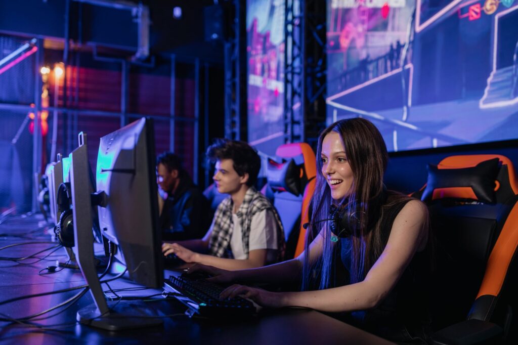 Players at computers on a lit esports tournament stage with a large screen behind