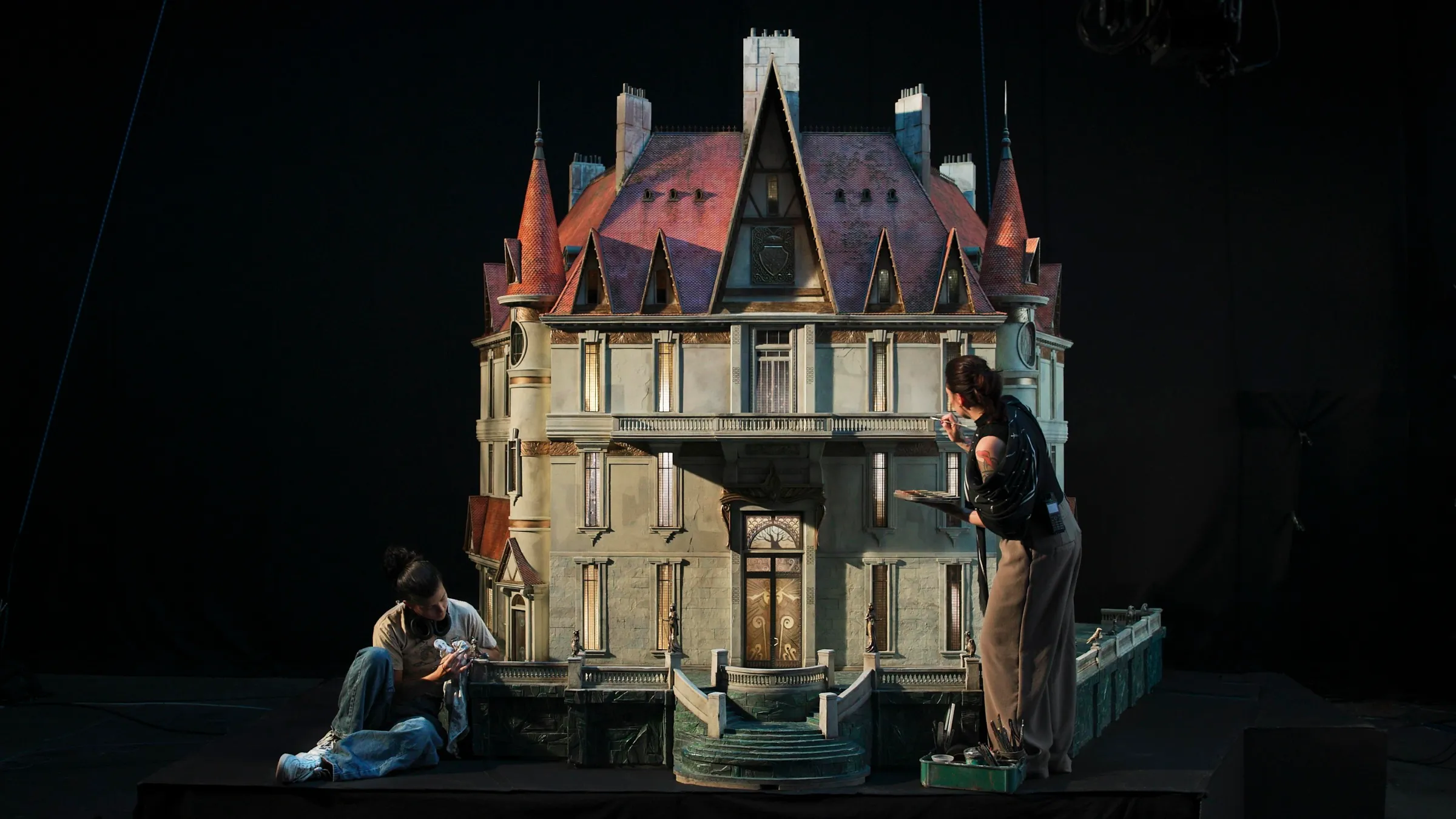 Two people work on a model of a grand-looking house that looks about 10 feet tall and will be used for an animated film.