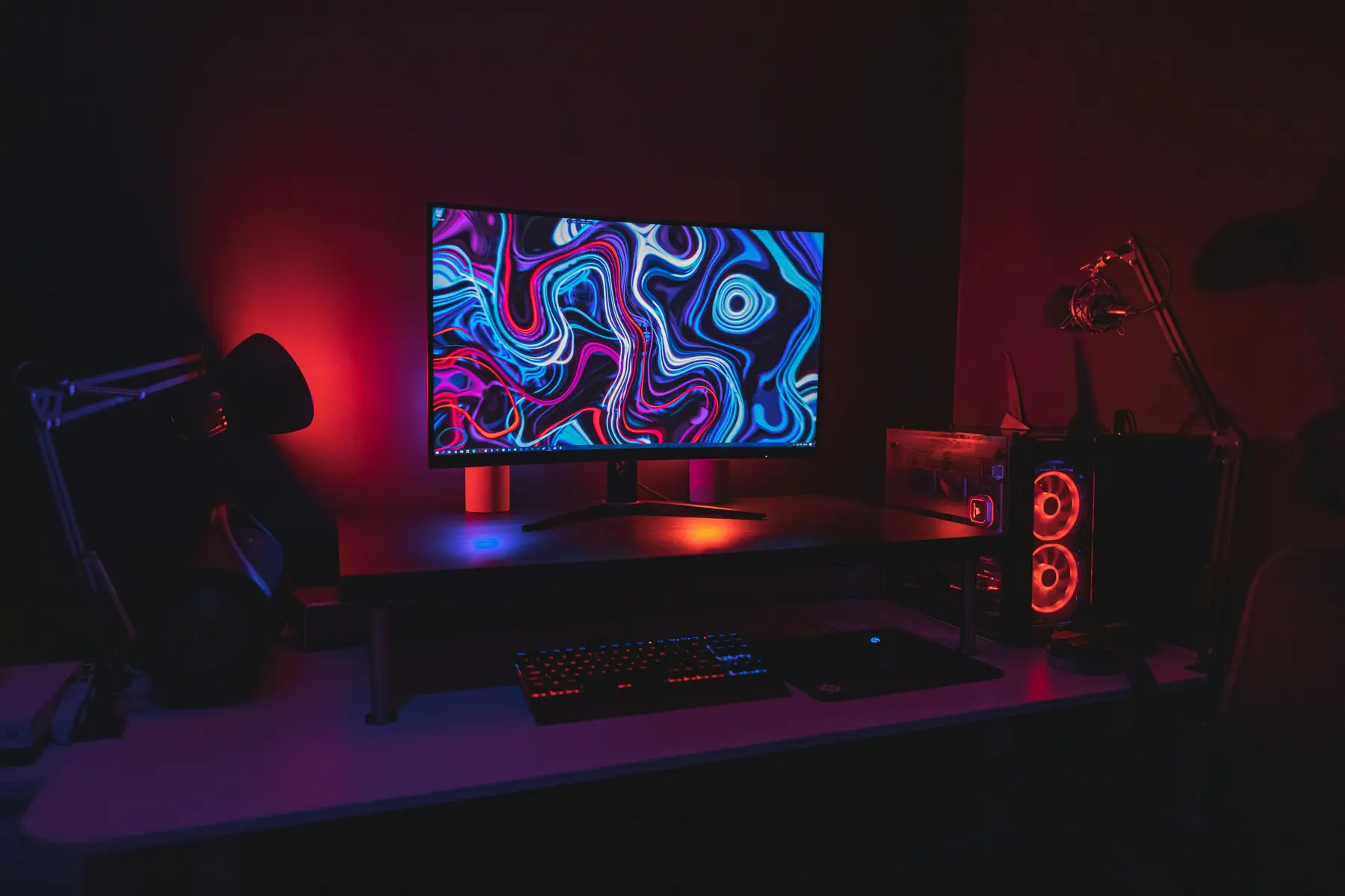 A gaming setup with a computer monitor displaying colorful abstract art, a keyboard, and a microphone
