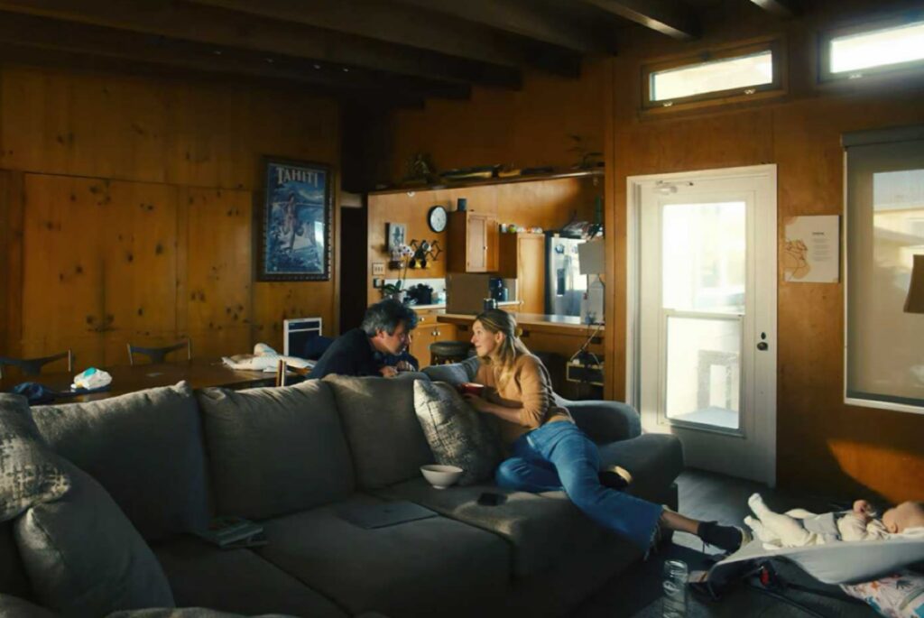 woman seated on couch, staring into the eyes of a man leaning over the back of the couch