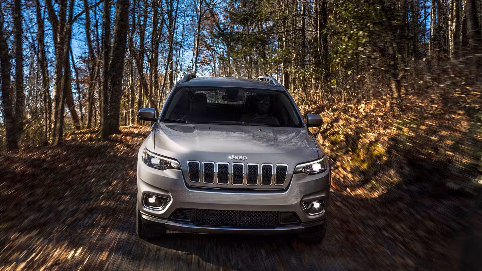 Front action shot of 2020 Jeep Cherokee driving through woodland