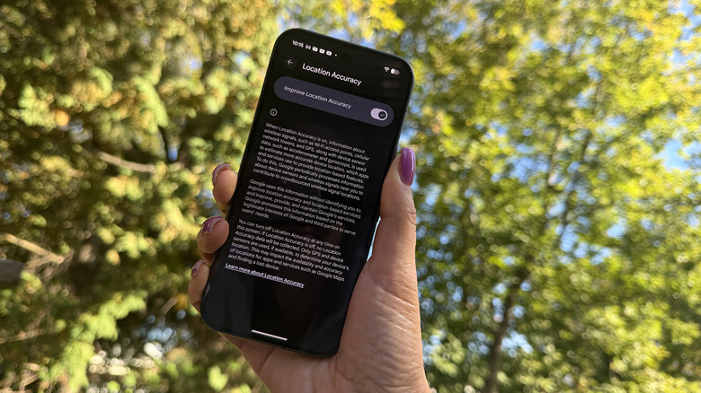A hand holding a Google Pixel 11 Pro showing the Location Accuracy setting.