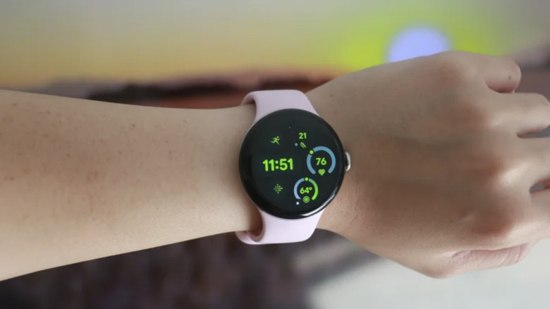 Photo of a person's wrist equipped with a Google Pixel Watch 3. The band is pale pink and the watch face shows the time and basic biometrics in green.