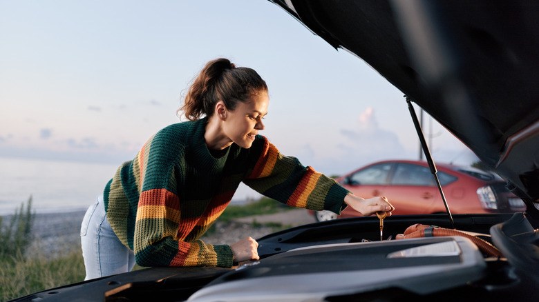 A woman checking fluid levels under the hood of a car using a dipstick