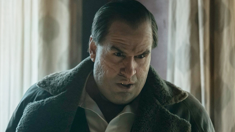 Colin Farrell as Oz Cobb wearing a winter coat and standing in front of a window in The Penguin