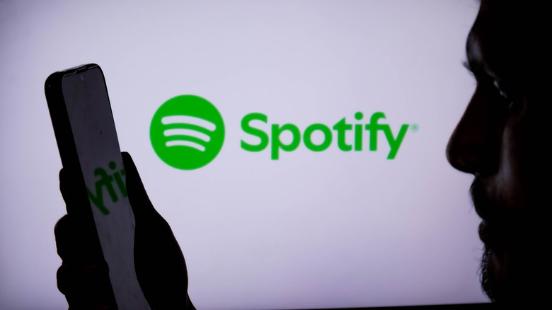 A person looking at a phone, illuminated by a Spotify logo in the background.