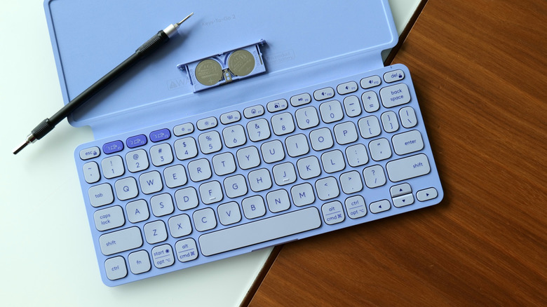 A small screwdriver sits atop a portable Logitech keyboard, with two button batteries exposed.