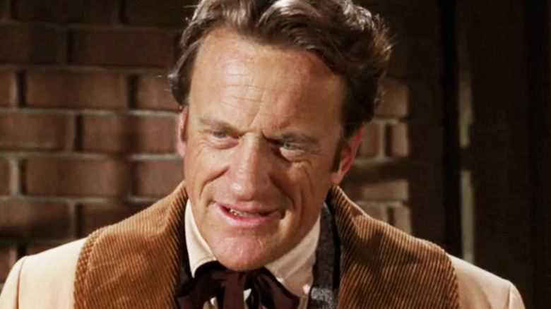 James Arness' Matt Dillon is seen in closeup standing in front of a brick wall in Gunsmoke