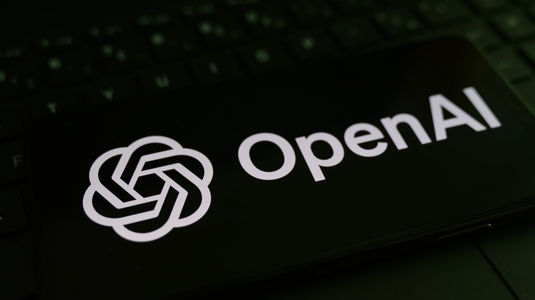 The OpenAI logo on a phone laying on a keyboard.