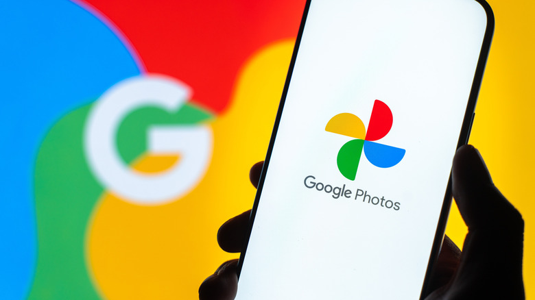A hand holding a phone that displays the Google Photos app. A Google logo is in the background.
