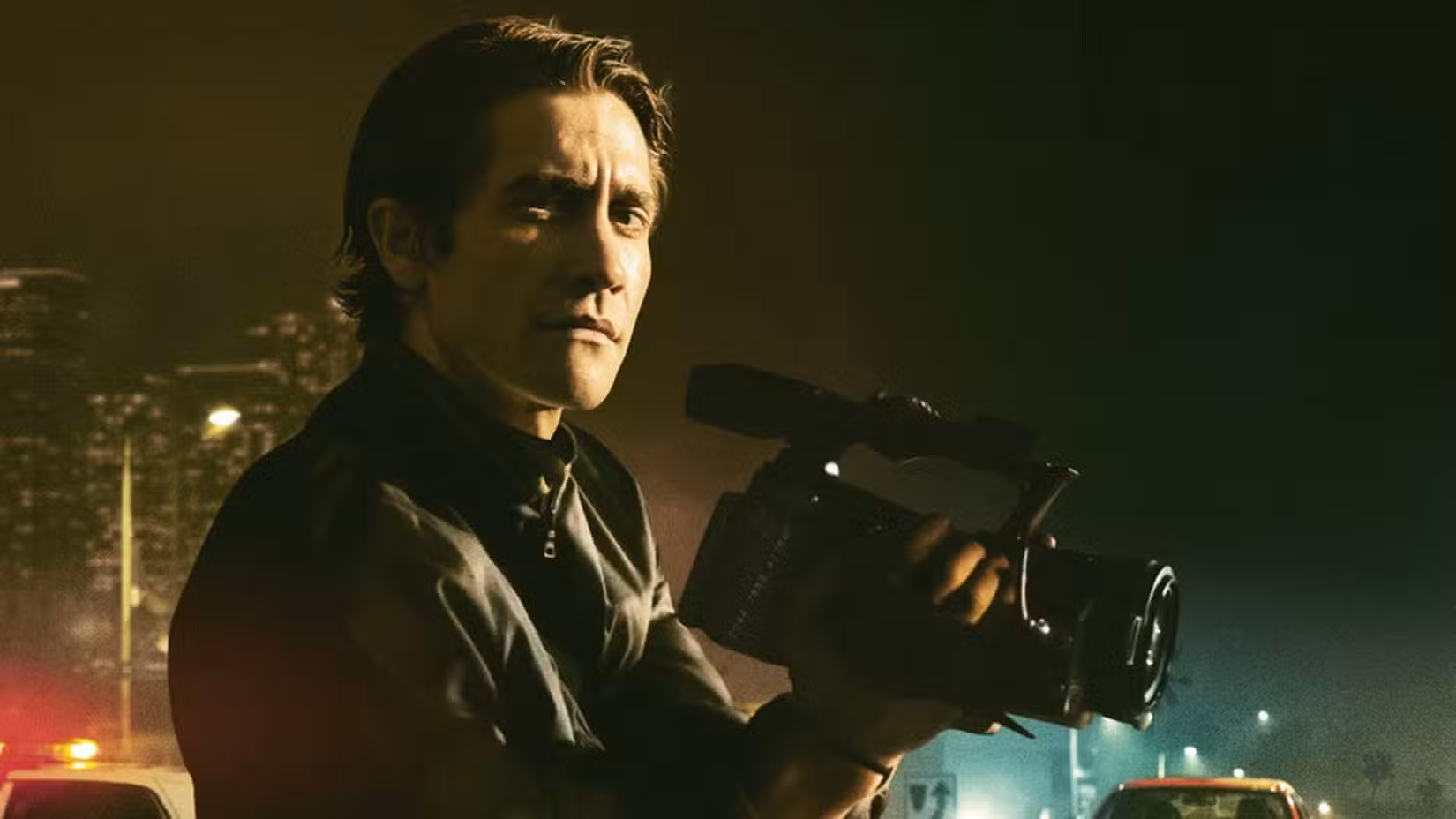 Jake Gyllenhaal holds a camera against the backdrop of the city in Nightcrawler. 