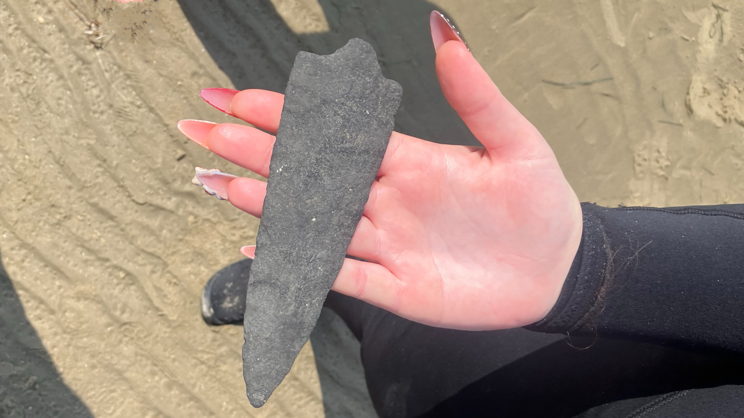 a person with light skin and long manicured nails holds a stone spearpoint in their open palm