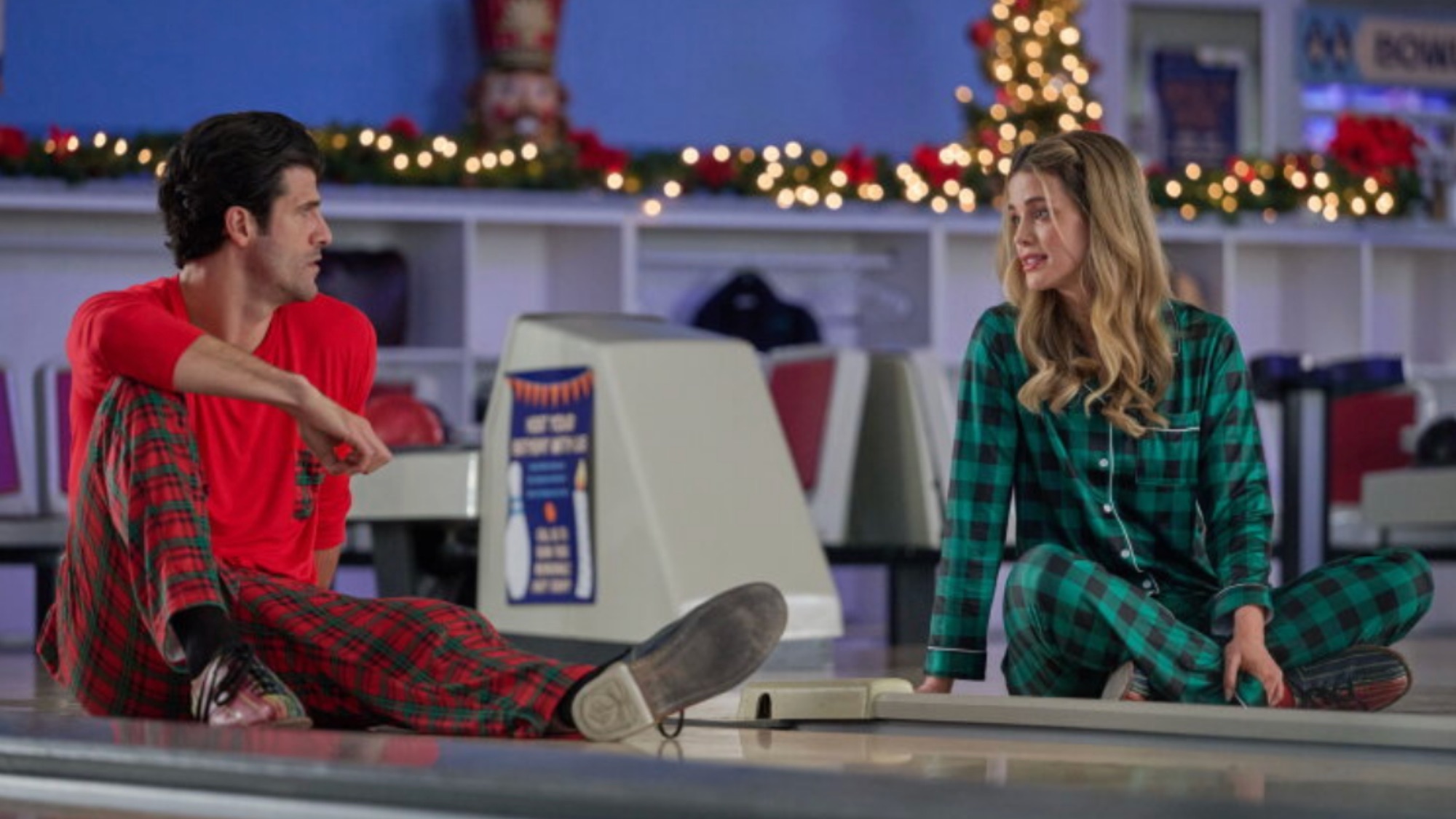 Audrey Newbrough and Franco Lo Presti wearing pajamas sitting in a bowling lane in Winter Wonderlanes