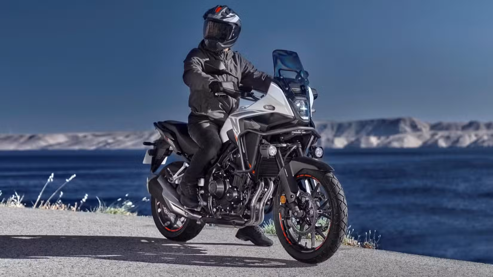 Rider sitting on a pearl white 2026 Honda NX500 in front of a lake