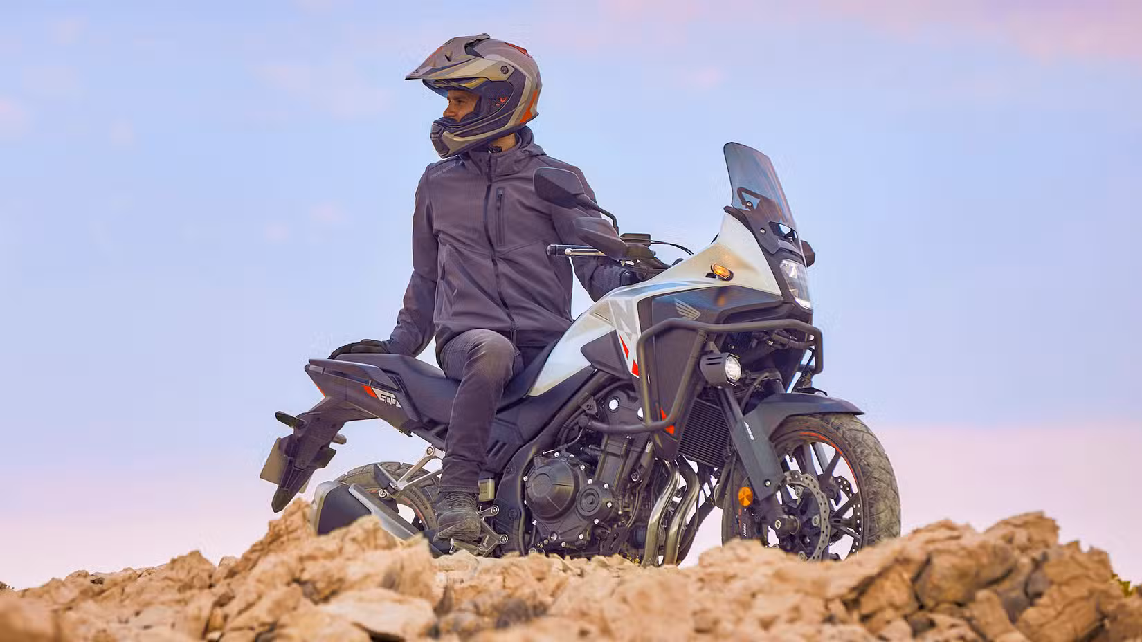 Rider sitting on a Honda NX500 atop a rugged rock hill