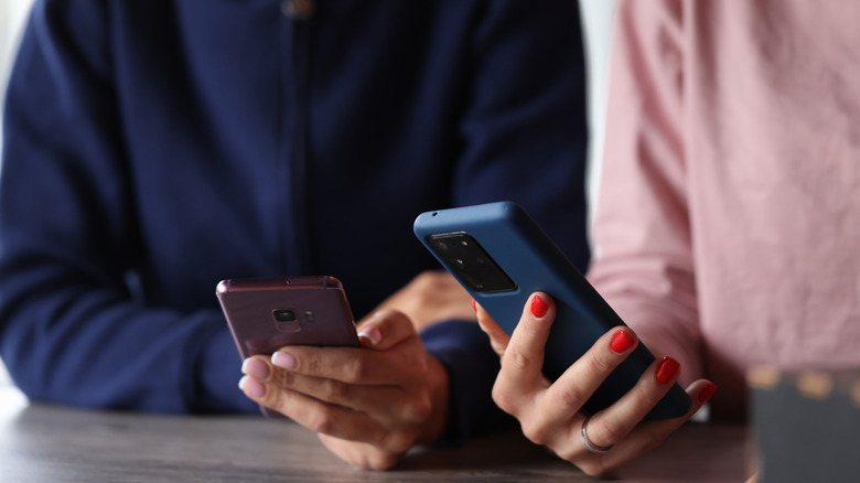 The hands of two people holding phones at a table.