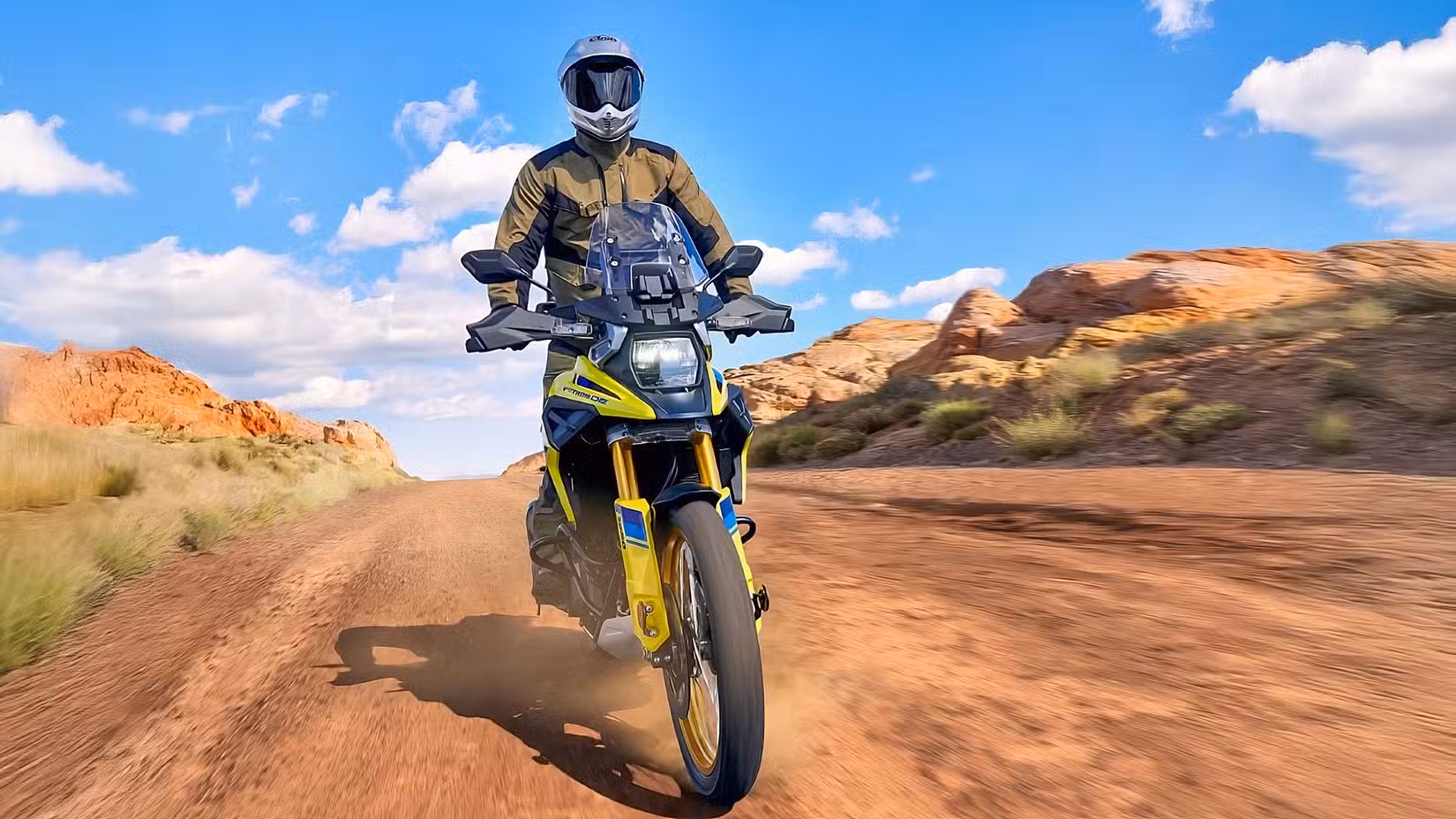 Suzuki V-Strom 1050DE with rider standing and riding on a dirt road