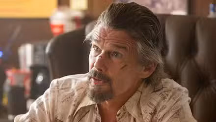 Ethan Hawke as Lee Raybon with a cut on his upper left cheek sitting at a desk in The Lowdown