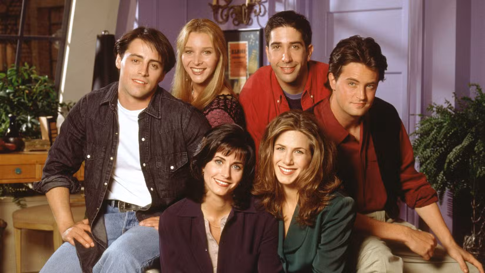 The main cast of Friends smiling at the camera in Monica's living room.